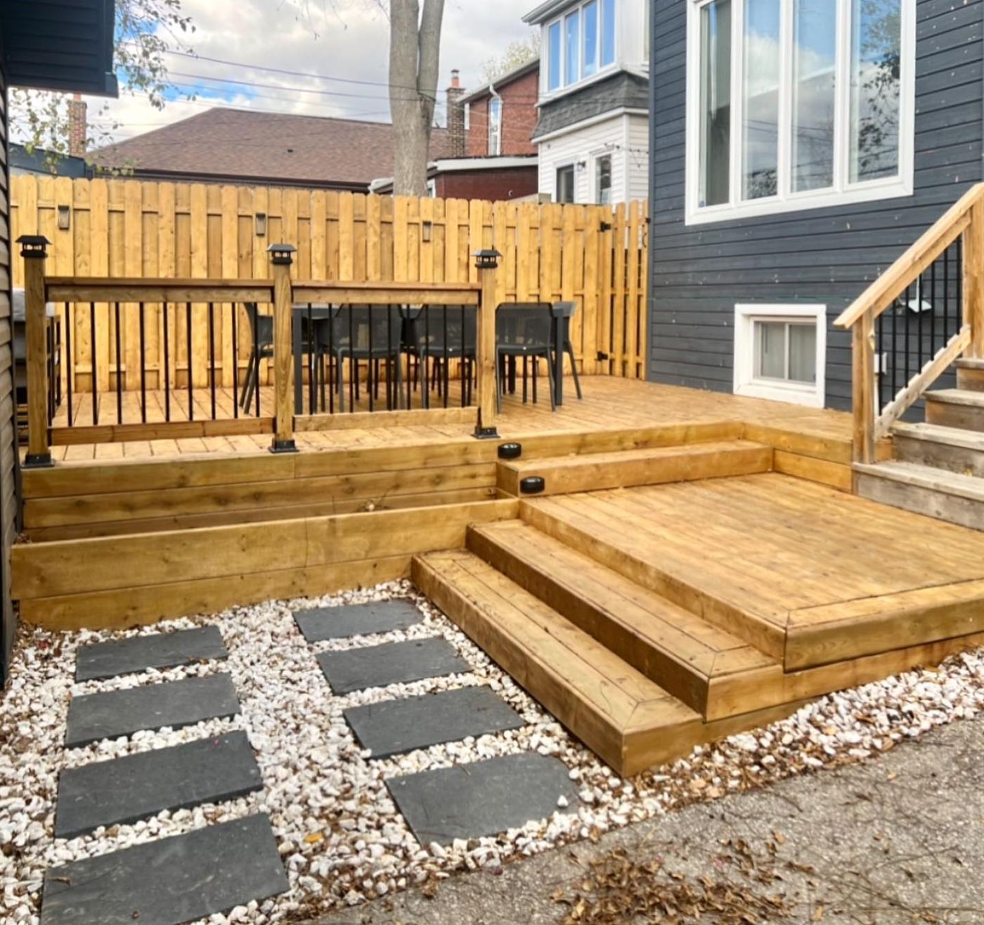 Multi-level cedar-tone deck with wide wraparound steps, black balusters and a stepping-stone path