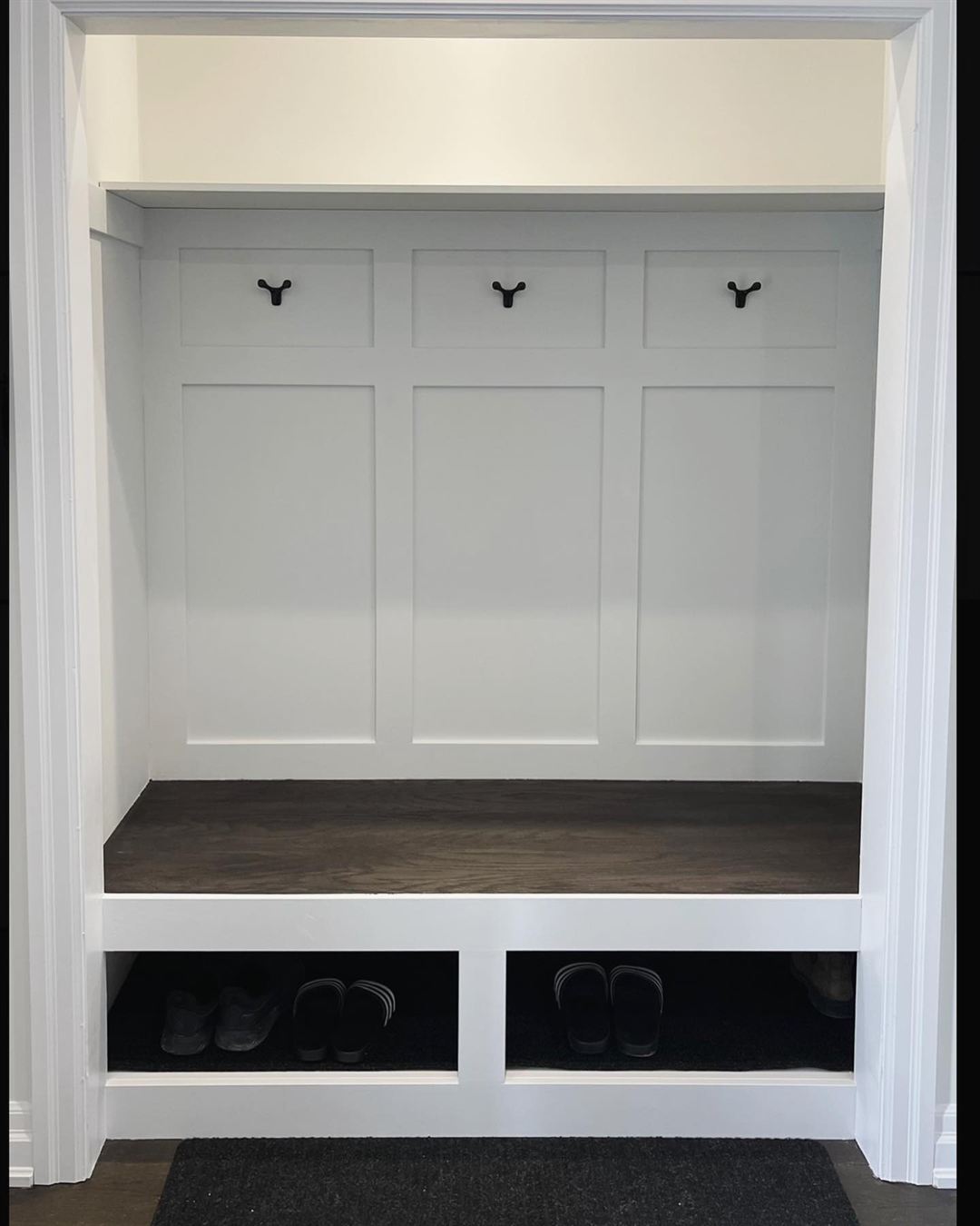 Built-in mudroom with Shaker panels, coat hooks, a stained bench and shoe cubbies